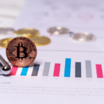 A gold Bitcoin coin resting on a line graph with a black pen beside it.
