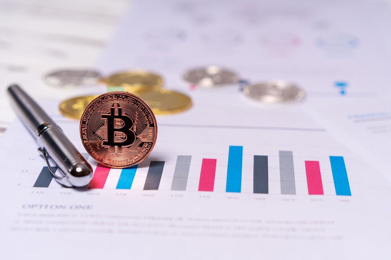 A gold Bitcoin coin resting on a line graph with a black pen beside it.