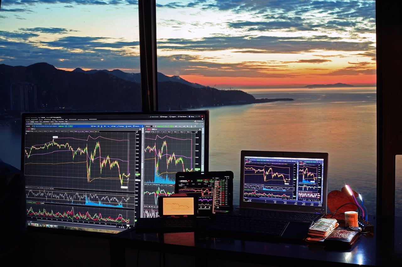 Multiple screens displaying financial charts and data with a scenic sunset view in the background.