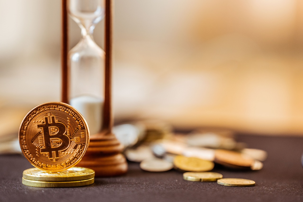 A Bitcoin coin standing upright with an hourglass in the background.