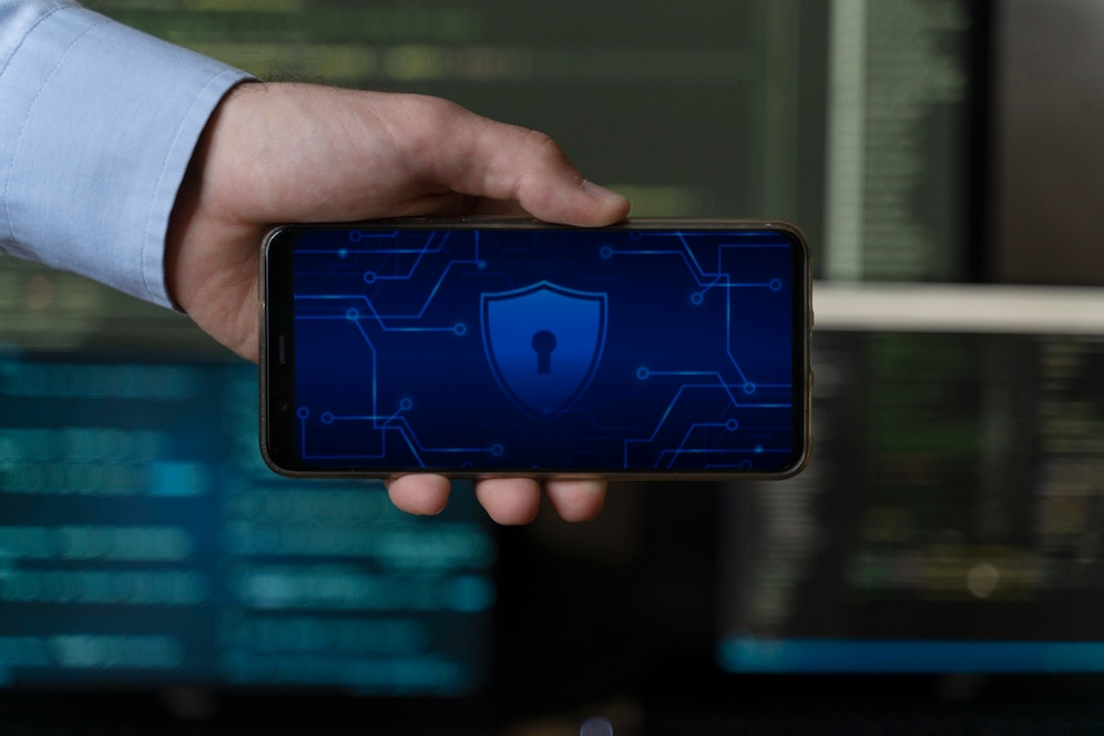 A person holding a smartphone with a security shield icon displayed on the screen, representing digital asset security.