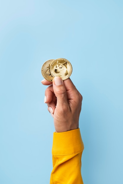 Hand holding two coins, one with the Dogecoin symbol and the other with the Bitcoin symbol.