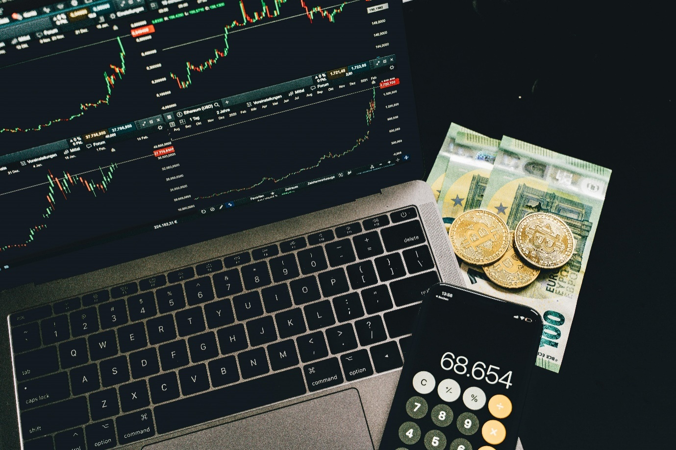 Bitcoin and paper money beside a cellphone and laptop