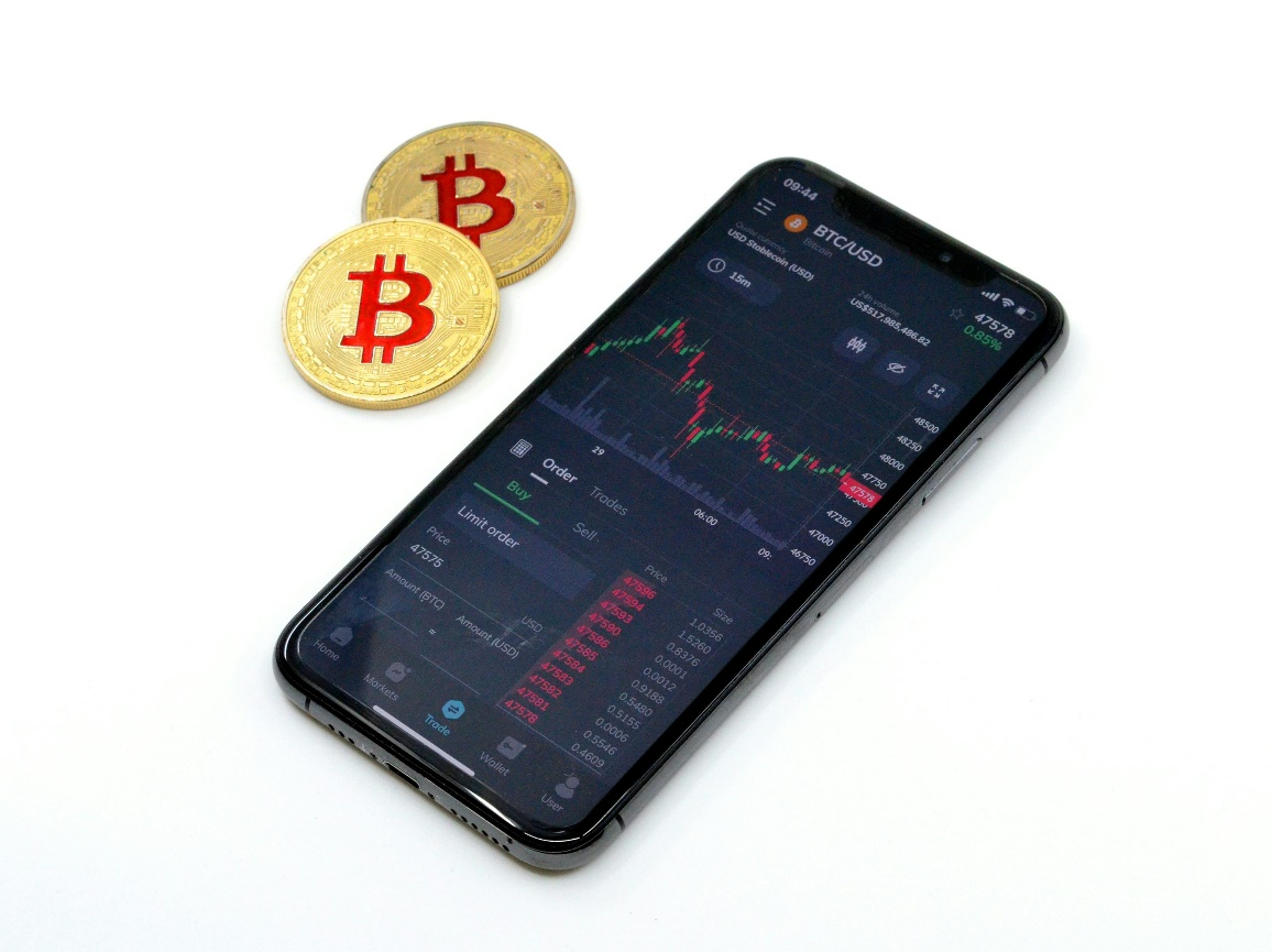 Smartphone displaying a Bitcoin trading graph with physical Bitcoins nearby.