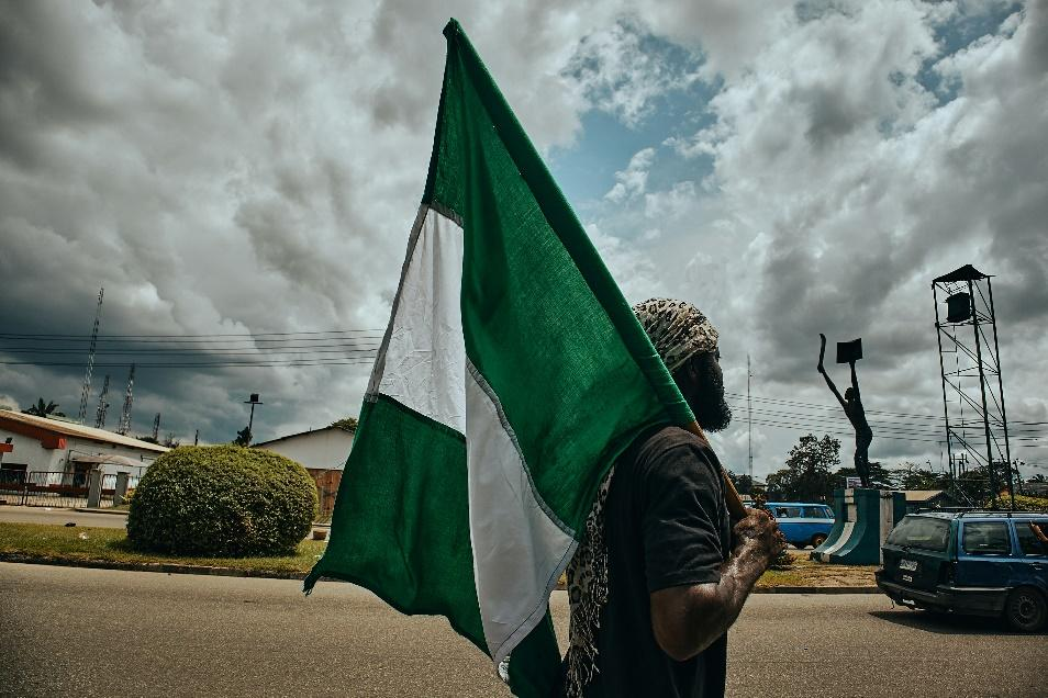 A man in Nigeria walks down a street carrying the Nigerian flag.