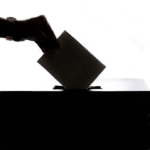 A silhouette of a hand dropping a ballot into a ballot box.