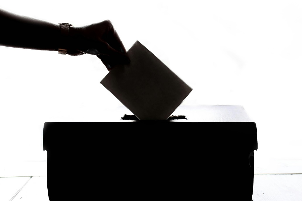 A silhouette of a hand dropping a ballot into a ballot box.