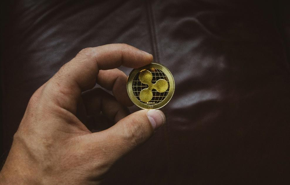 A person's hand holding a gold Ripple coin.