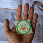 A hand holding an "I Voted" sticker.