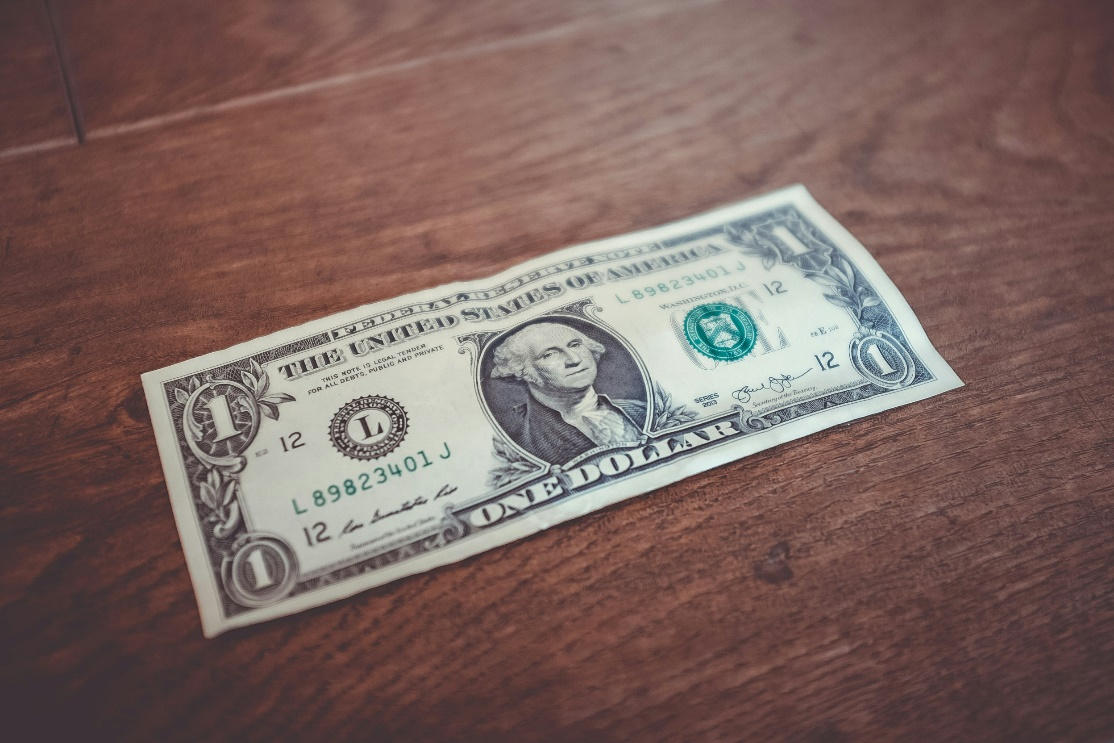 A single US dollar bill resting on a wooden surface.