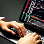 A person's hands typing on a laptop keyboard with a cryptocurrency trading chart displayed on the screen.