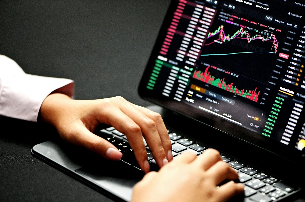 A person's hands typing on a laptop keyboard with a cryptocurrency trading chart displayed on the screen.