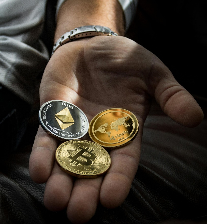 A person's hand holding various cryptocurrencies including Bitcoin, Ethereum, and Ripple.