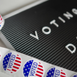 Voting Day sign next to red, white, and blue voting pins, symbolizing political influence in the 2026 midterm elections.