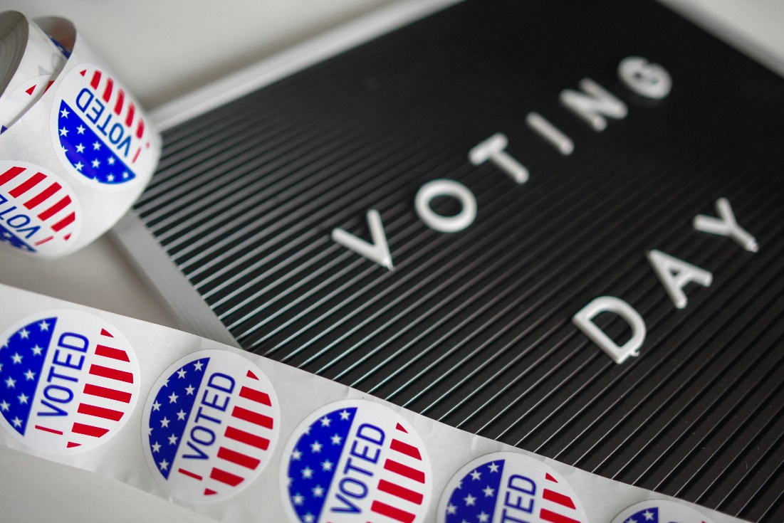 Voting Day sign next to red, white, and blue voting pins, symbolizing political influence in the 2026 midterm elections.