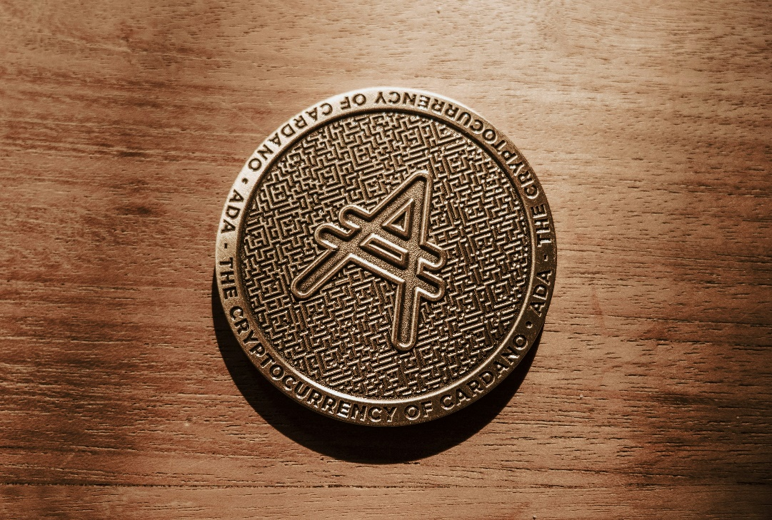 A close-up, top-down shot of a gold-colored Cardano (ADA) coin.