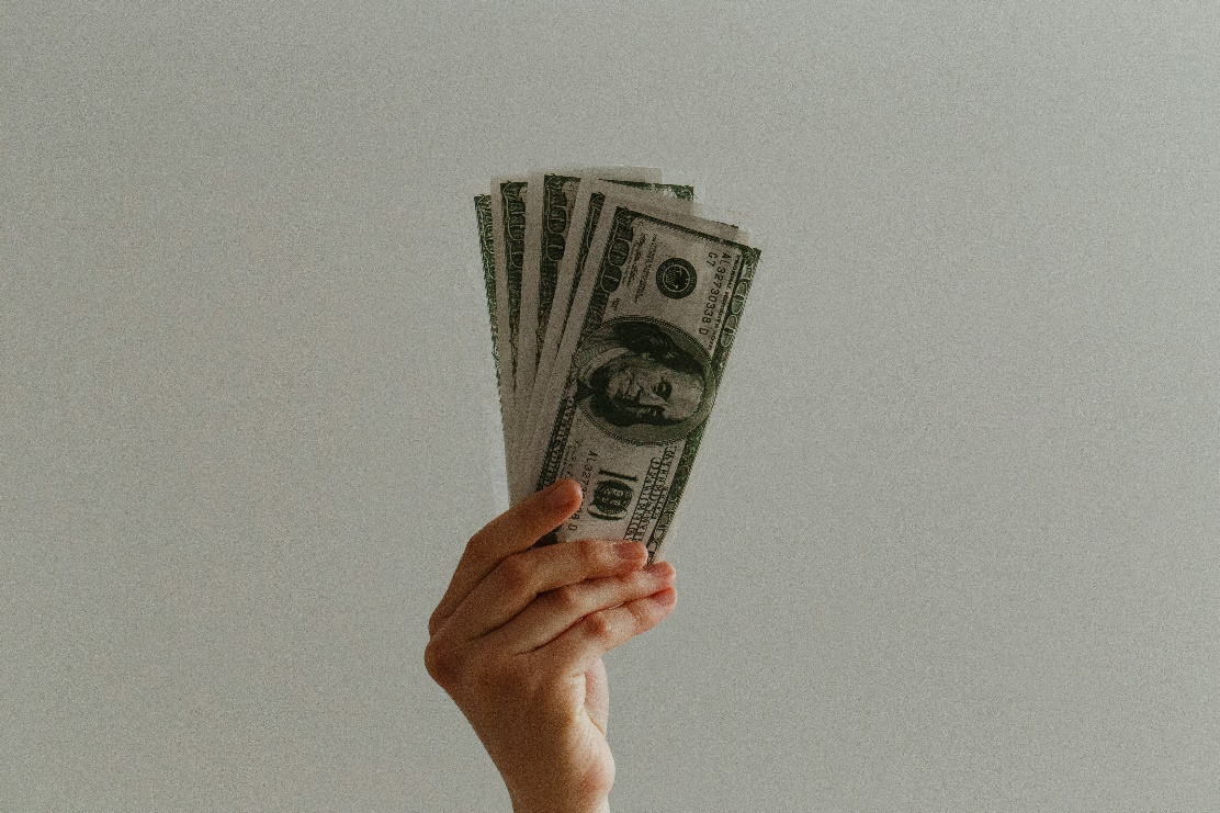 A hand holding a stack of US dollar bills against a plain background.