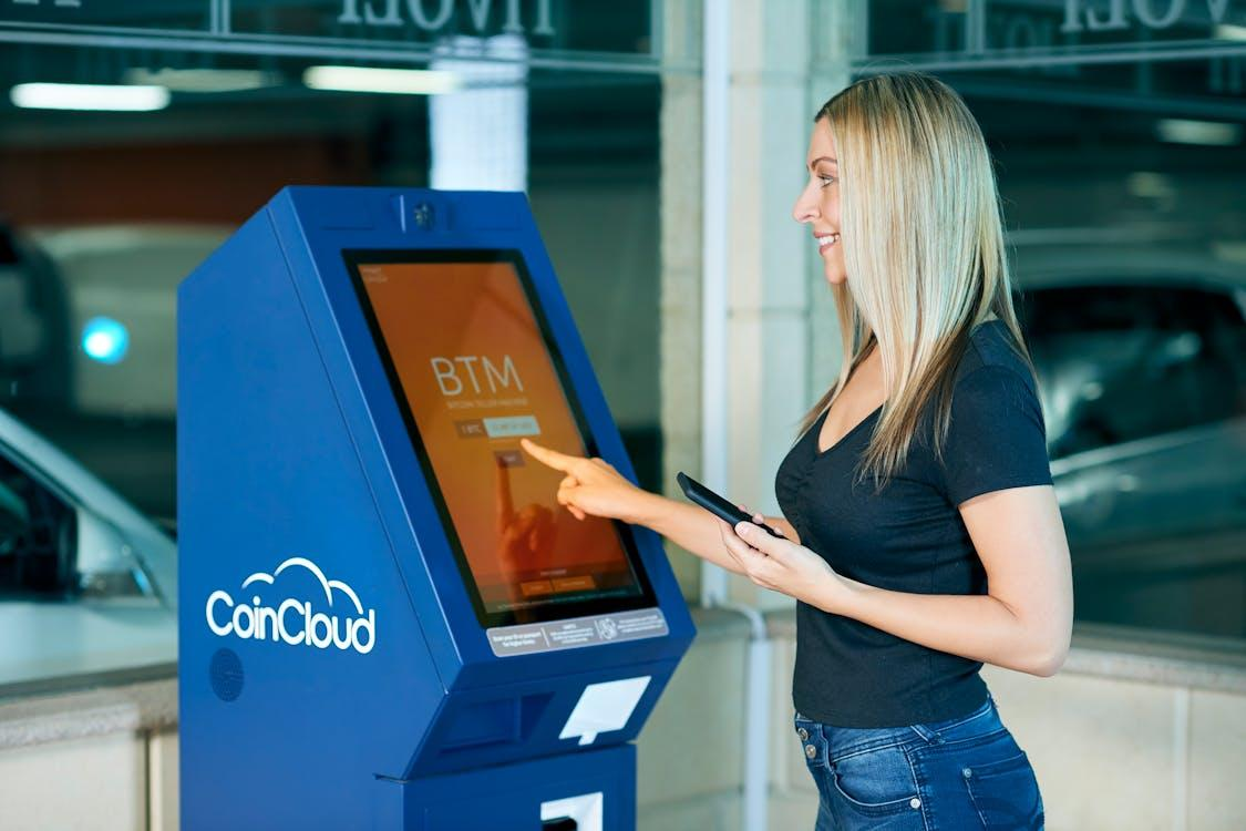 a blonde haired woman in black top using atm