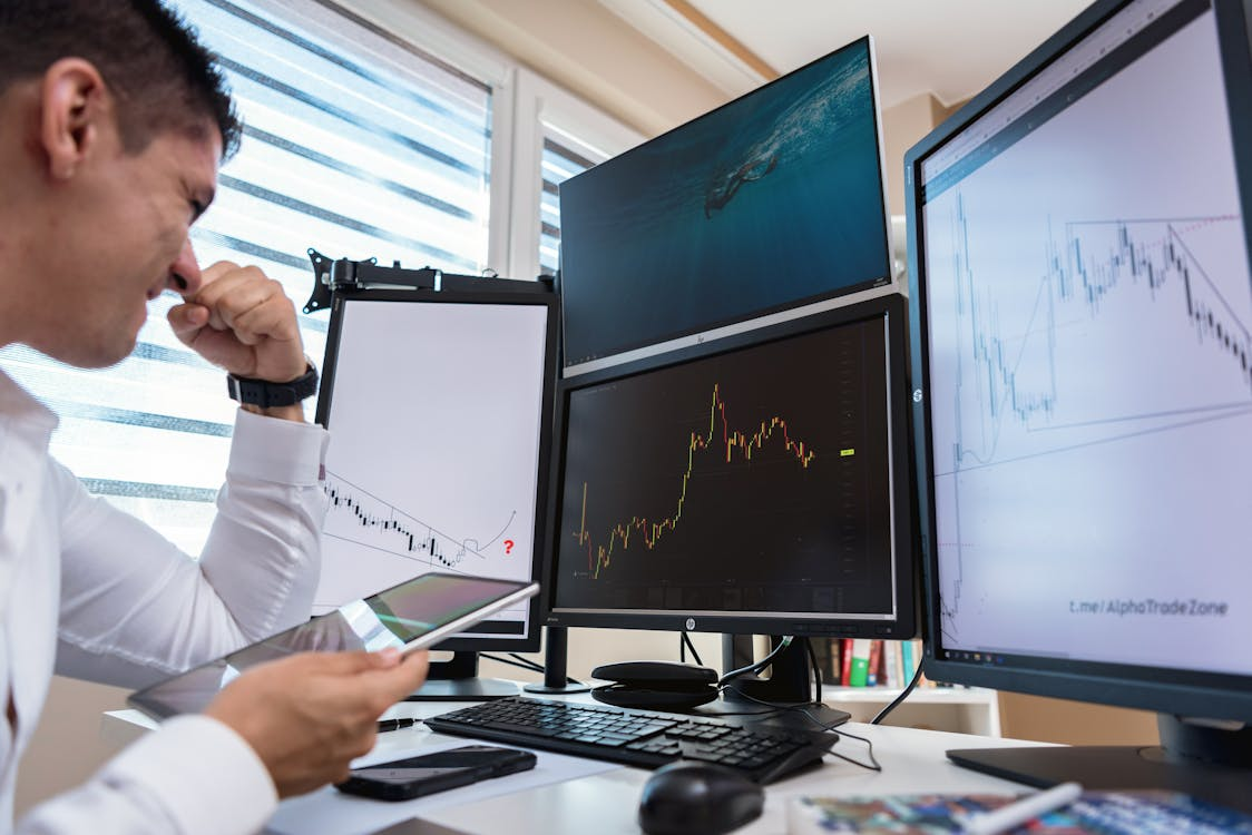 A man in white long sleeves looking at the line graph on the monitors.
