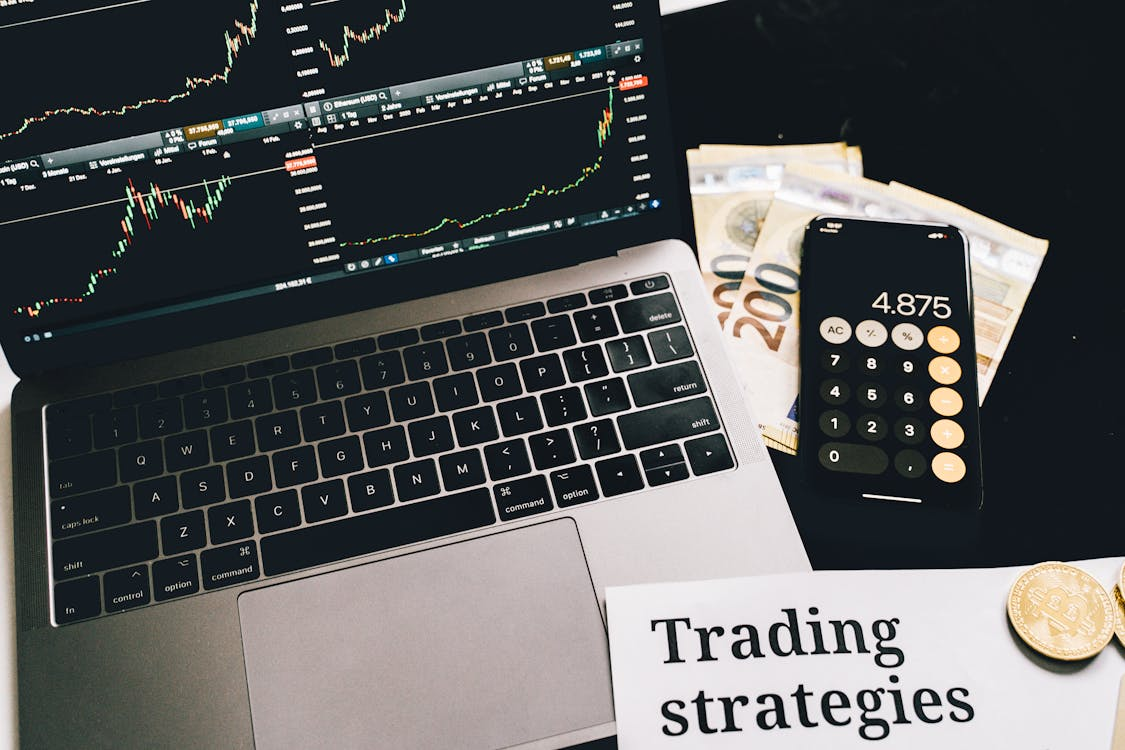 kenson Investments | Portfolio Diversification with Digital Assets – Long-Term Allocation Considerations A laptop with graphs on screen beside a smartphone on paper money.