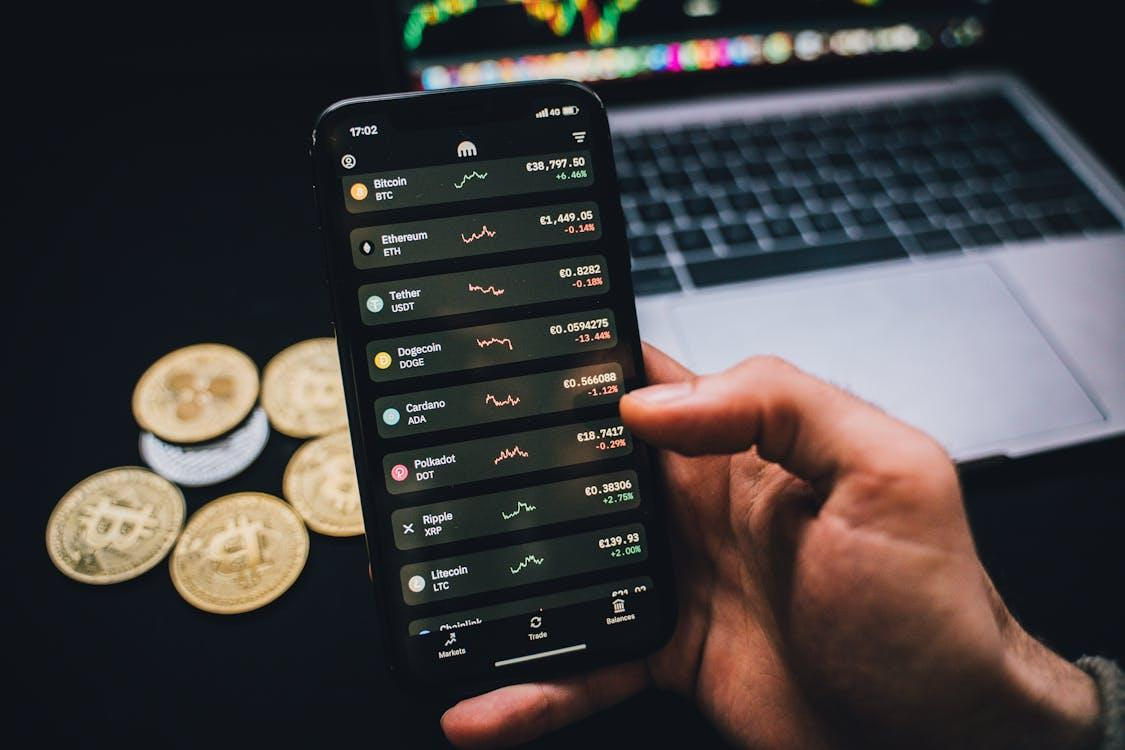 kenson Investments | Crypto Got Rattled: Bitcoin’s Drop Wipes Out $500M in Longs, Dogecoin and ADA Tank person holding a smartphone with trading graphs