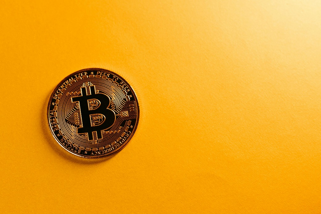 Gold Bitcoin placed on a bright yellow background.