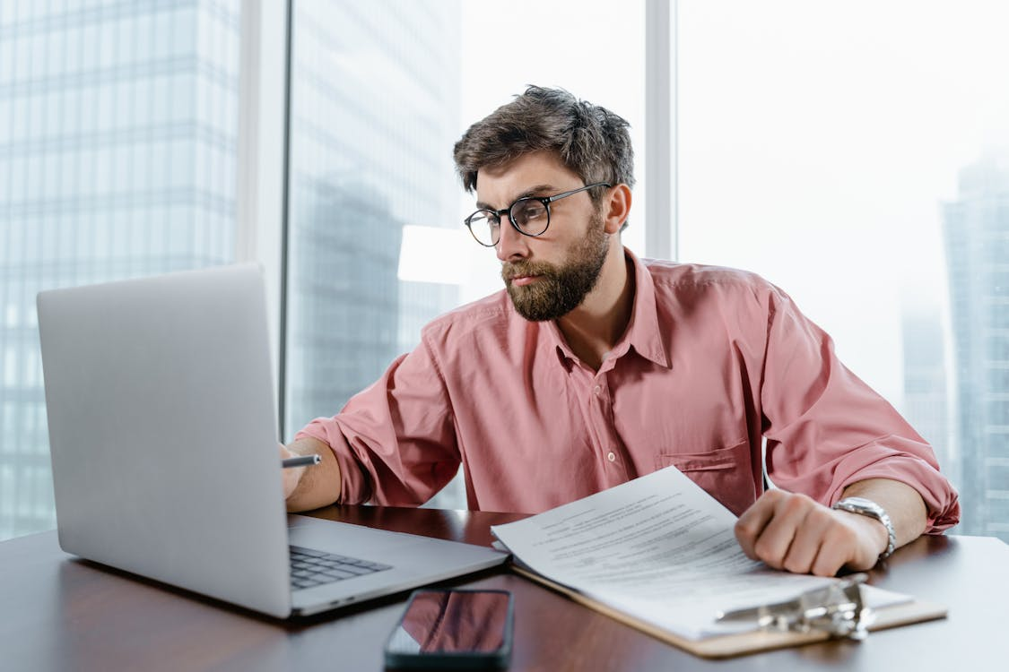 Man in red dress shirt wearing black-framed eyeglasses using MacBook Air.