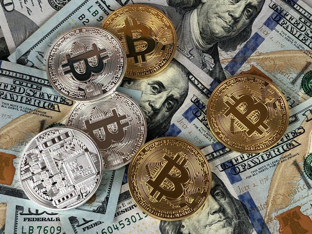 kenson Investments | JPMorgan’s Bitcoin Miner Upgrade: What It Really Means for the Industry Several gold and silver-colored physical Bitcoin tokens scattered over multiple U.S. one hundred dollar bills.