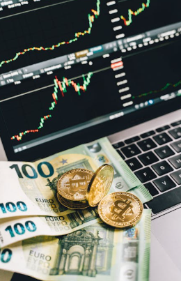 kenson Investments | Bitcoin Doesn’t Blink: How Crypto Kept Its Cool Amid Geopolitical Mayhem Gold-colored Bitcoin tokens and several 100 Euro banknotes placed on a laptop keyboard with trading charts displayed on the screen.