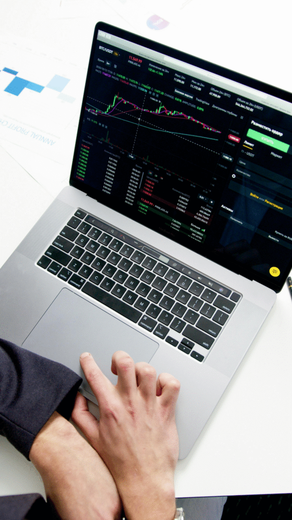 kenson Investments | GameStop Reloads Its War Chest—Is Bitcoin the Next Boss Fight? A person’s hand on a MacBook trackpad with a cryptocurrency exchange interface displayed on the screen.