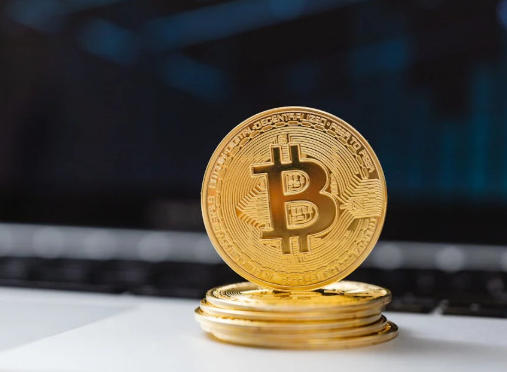 kenson Investments | When the Leverage Breaks: One Trader’s $200M Bitcoin Loss and the Billion-Dollar Liquidation Storm A stack of gold-colored physical Bitcoin tokens placed on a white surface in front of a blurred laptop keyboard.