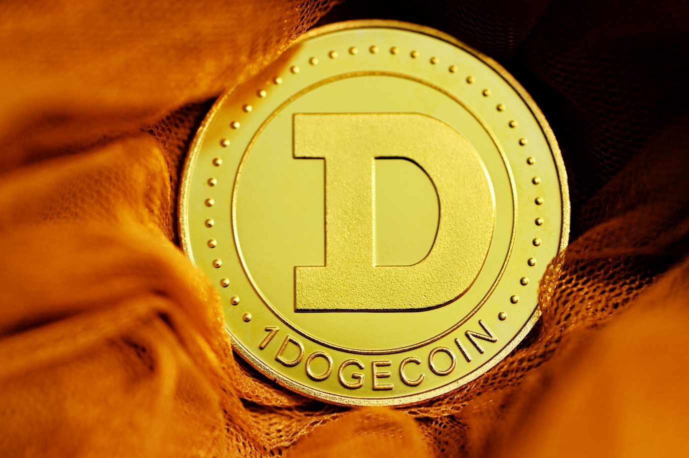 kenson Investments | Dogecoin Dips After the Hype – ETF Talk Isn’t Enough to Keep the Rally Going A gold-colored physical Dogecoin token marked “1 DOGECOIN” resting on an orange fabric background.