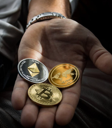 kenson Investments | When the Leverage Breaks: One Trader’s $200M Bitcoin Loss and the Billion-Dollar Liquidation Storm A person’s open hand holding three physical cryptocurrency tokens representing Ethereum, Bitcoin, and a world map design.