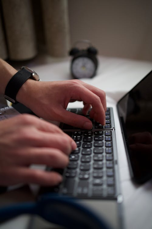 kenson Investments | Paul Tudor Jones Just Dropped a Bitcoin Bomb—And We’re Listening A person typing on a laptop keyboard with an analog alarm clock blurred in the background.