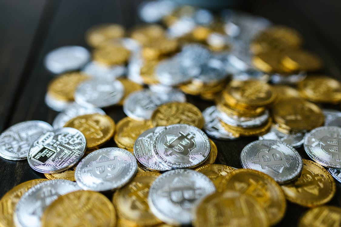 kenson Investments | ADA Defies Whale Waves – Enterprise Buzz Keeps Cardano Steady A scattered pile of silver and gold-colored physical Bitcoin tokens spread across a dark wooden surface.