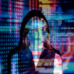 A woman standing in front of a screen with multicolored digital code and binary numbers projected onto her face and clothing.