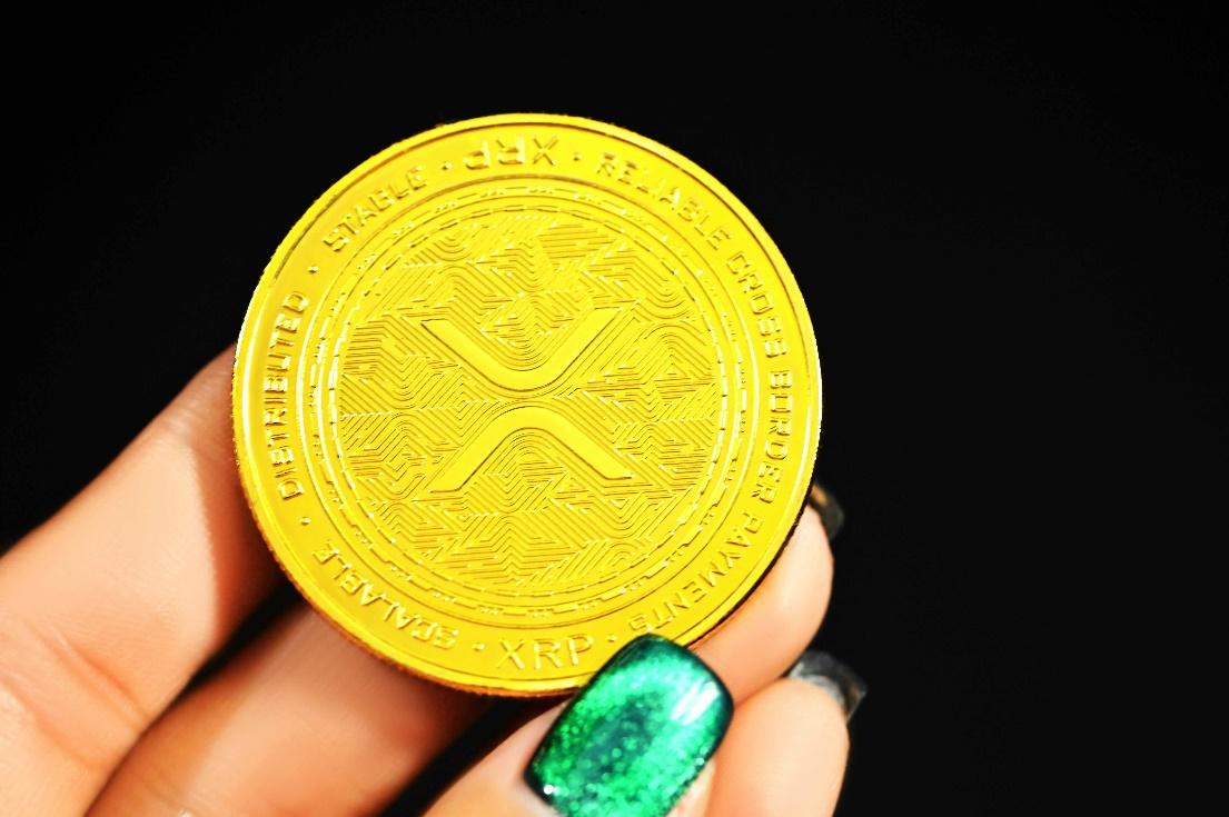 A hand holding a shiny golden XRP cryptocurrency coin.