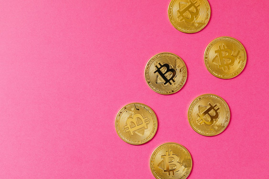 Round cryptocurrency coins displayed on a pink surface symbolising Bitcoin’s return to luxury fashion payments in 2025.