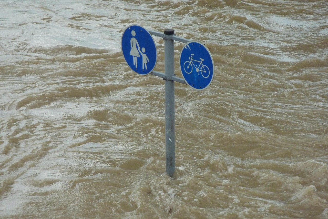 Warning sign during severe floods showing downfall and heavy water flooding in urban area.