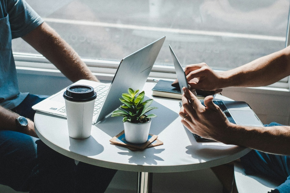 Two professionals collaborating with laptops and devices at a small table.