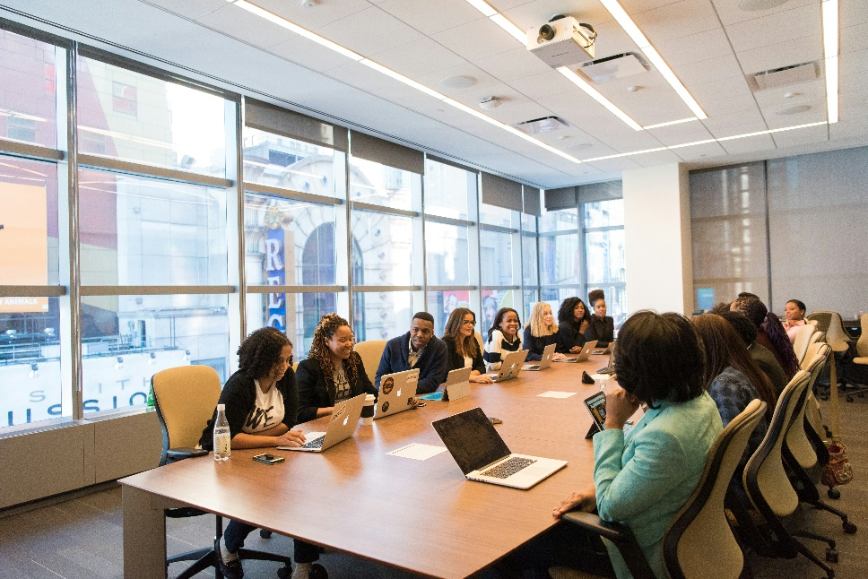 A large group of professionals seated around a conference table with laptops.