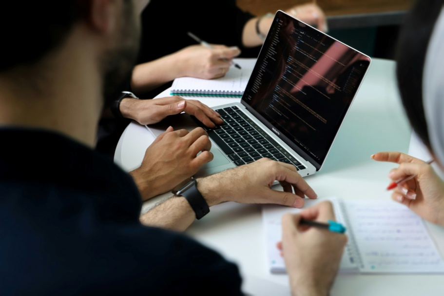 Team of professionals reviewing blockchain code and infrastructure requirements on a laptop during a technical evaluation session.