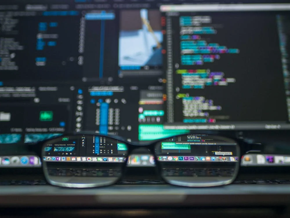 Computer code displayed on monitors reflected through eyeglasses