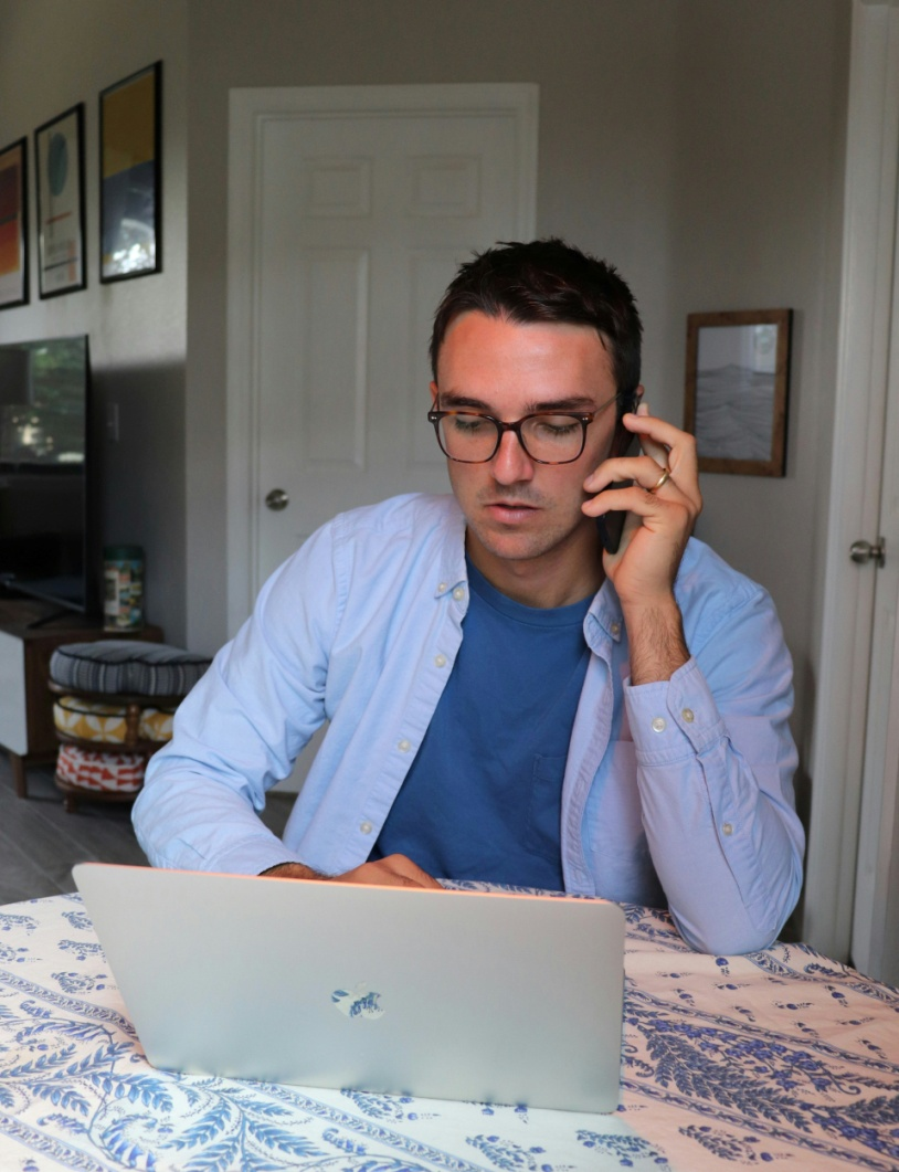 An individual working on a laptop while speaking on a phone.