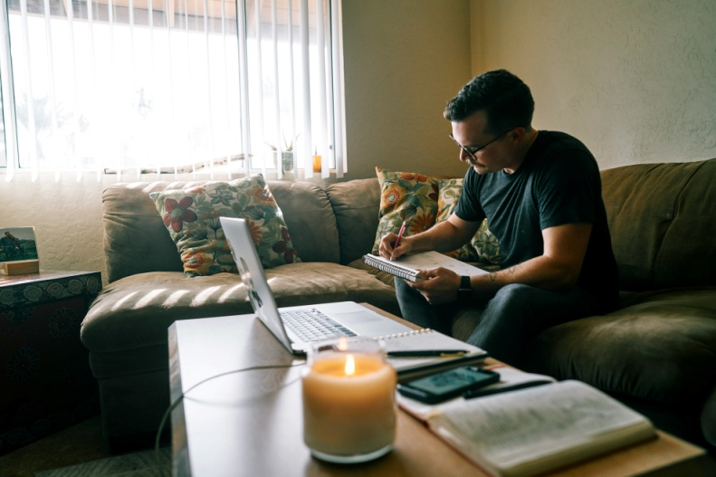 An individual reviewing notes and a laptop at home.
