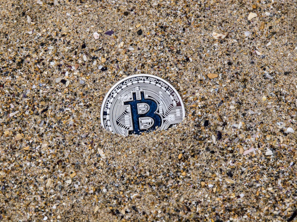 A single bitcoin partially buried in sand, symbolizing digital assets exposed to environmental and operational risks.