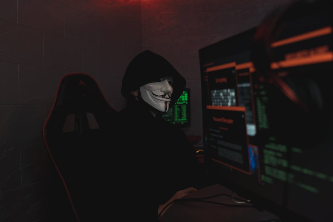 Person wearing a mask while using a device, representing the threat of phishing and social engineering in digital asset management.