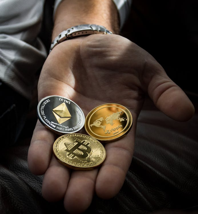 Close-up of three coins held in a person’s hand, symbolizing ownership and management of digital assets.