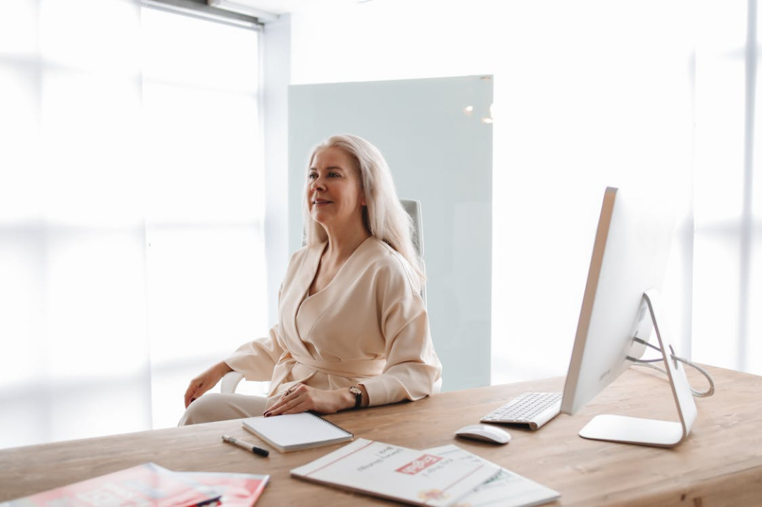 Woman sitting next to a table with a laptop and papers, symbolizing active learning and engagement in digital asset management.
