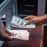 kenson Investments | Stablecoins or Tokenized Deposits: Which Money Belongs on Institutional Settlement Rails? Hands exchanging currencies across a bank counter